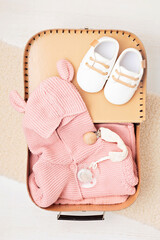 Wall Mural - A cozy display of newborn essentials featuring hand-knit pink sweater, hat, pacifier, and wooden bird toys neatly arranged inside an open suitcase