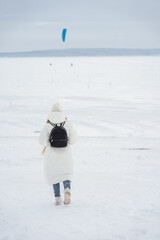 Wall Mural - Winter photo of a young girl in a white jacket and with a backpack walking through snow and ice on a frozen river, snowy desert landscape