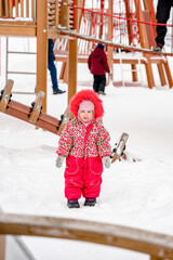 Wall Mural - A little todd girl in a red down jacket with fur on a playground in winter on a sunny day. Saint Petersburg, Russia - 10 Feb 2024