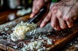 Close-up shot of hands chopping mozzarella cheese with a kitchen knife on a wooden board with shavings scattered