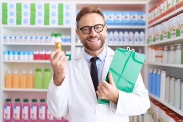 Poster - Middle age man with beard working at pharmacy drugstore holding pills smiling with a happy and cool smile on face. showing teeth.