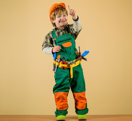 Wall Mural - Cute kid repairman in protective helmet with toolbelt of toy tools for building. Happy child boy in uniform and hard hat with builder tools set. Little child builder playing with toy tools for repair.