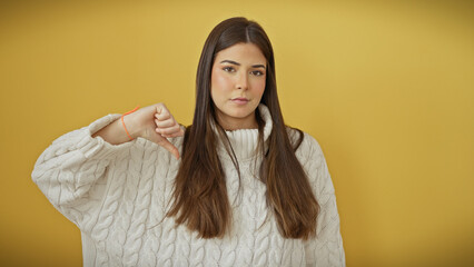 Wall Mural - A young hispanic woman gives a thumbs-down gesture against an isolated yellow background, suggesting dissatisfaction.