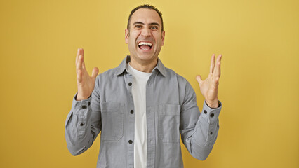 Wall Mural - A cheerful hispanic man gesturing excitement against a vibrant yellow wall, expressing joy and happiness.