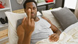 An african american man in bed displaying displeasure with a rude gesture indoors