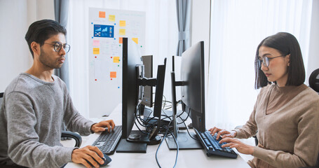 young adult asian male, female software developer coding program on desktop computer. man, woman wor