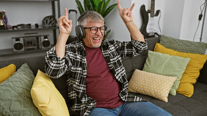 Poster - A joyful, middle-aged man with grey hair enjoys music on headphones in a cozy living room