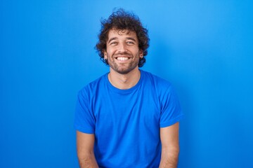 Wall Mural - Hispanic young man standing over blue background with a happy and cool smile on face. lucky person.