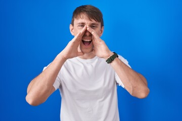 Sticker - Caucasian blond man standing over blue background shouting angry out loud with hands over mouth