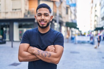 Young latin man standing with arms crossed gesture at street