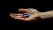 Red and blue pills held in a hand, isolated on a black background
