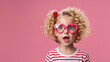Little blonde child with heart shaped eye glasses on pink background with copy space. Happy childhood, Valentines day celebration holidays.
