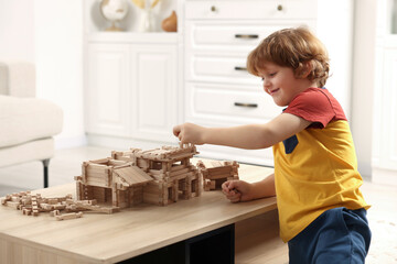 Sticker - Cute little boy playing with wooden construction set at table in room. Child's toy