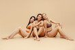 © Maria Vitkovska - Group beautiful smiling multiethnic women wearing sexy underwear  isolated on beige background. Attractive stylish fashion models sitting barefoot looking at camera. Natural beauty, body positive