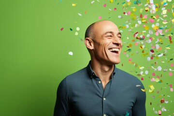 Wall Mural - Portrait of a happy mature man with flying confetti on a green background