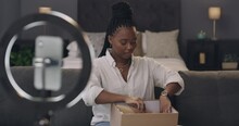 Young woman, unboxing and cellphone recording for social media on bed, fashion vlogger and talking on podcast. Black person, excited or heels review by influencer or smartphone on ring light in house
