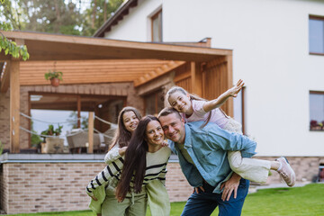 Wall Mural - Beautfiul young family standing in front their family home, enjoying together time.