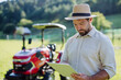 © Halfpoint - Farmer reading document in front of tractor on field. Grants, loans, funding opportunities for farmers.
