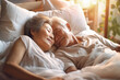 An elderly Asian man and woman are seen laying together on a bed, showing affection and intimacy