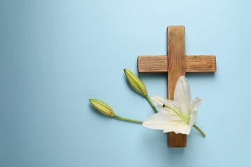 Wall Mural - Wooden cross and lily flowers on light blue background, top view with space for text. Easter attributes