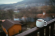 White cup with hot tea on wooden balcony with mountains view.