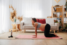 Pregnant woman practicing cow pose on yoga mat at home