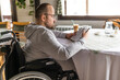 Paraplegic handicapped man in wheelchair is sitting at restaurant and reading book.