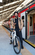 © Westend61 - Smiling man holding smart phone by bicycle near train at station