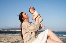 Smiling Woman Sitting On Sand And Playing With Baby Girl At Beach