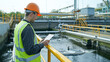 Environmental engineer in a reflective vest inspecting a wastewater treatment plant with a digital tablet.