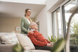 © Westend61 - Happy home caregiver with senior man sitting on sofa in living room
