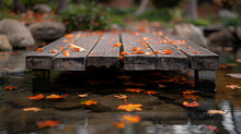 A Rustic Wooden Bridge, With Fallen Leaves Floating On The Water Below, During The Tranquil Transition Into Autumn