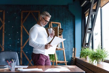 Wall Mural - Serious pensive thoughtful focused middle-aged casual entrepreneur accountant bookkeeper in office looking at income tax return papers and documents