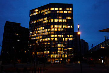 Wall Mural - Office building lights up the evening with windows glowing in the dusk, showcasing urban work life after hours