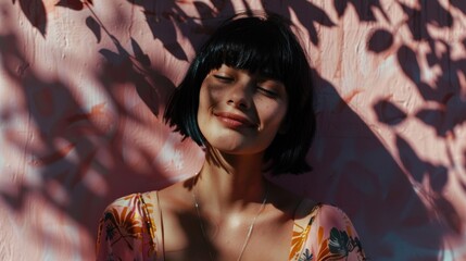 Wall Mural - A woman with closed eyes smiling wearing a floral top leaning against a pink wall with leaf shadows.