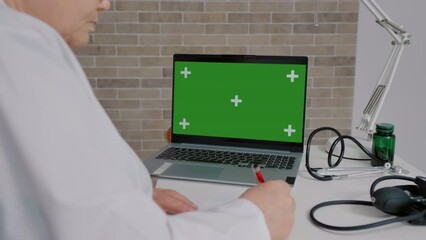 Woman doctor studying online on green screen chroma key laptop. Doctor passing a training online using laptop.