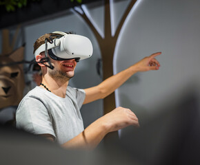 Teen man having fun in the natural history museum VR room, using virtual reality headsets, making various hand movements in the air.