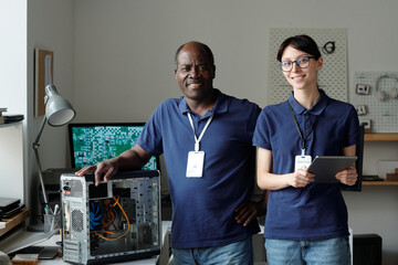 Poster - Two successful engineers of repair service center looking at camera while young woman using tablet and mature man touching processor
