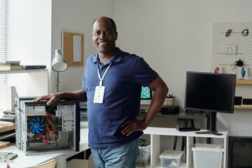 Poster - Happy experienced engineer of maintenance center looking at camera with smile and keeping hand on top of computer processor in office