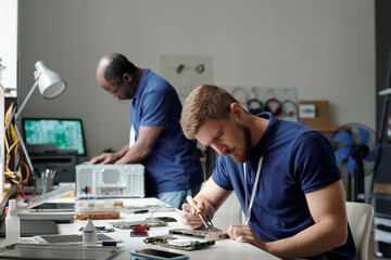 Poster - Young serious specialist of troubleshooting and repair service center with transmission tweezers bending over workplace with motherboard