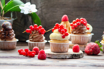 Wall Mural - Chocolate and vanilla cupcakes decorated with fresh berries on rustic wooden background