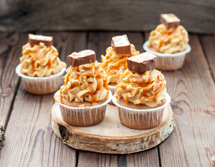 Wall Mural - Delicious chocolate cupcakes with peanut butter frosting, chocolate bites and salted caramel sauce on rustic wooden background