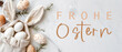 Frohe Ostern Konzept Feiertag Grußkarte mit deutschem Text - Geschenkbeutel aus Stoff mit Osterhasenohren und Ostereier auf weissem Tisch, Draufsicht