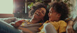 Exuberant laughter fills the room as an African American mother and daughter playfully recline at home.