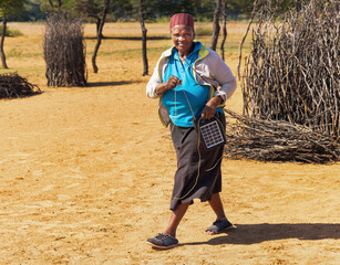 village old african woman using a solar panel with radio, to recharge phones and light, donated by a charity NGO, to improve life in rural areas