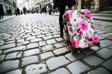 Fototapeta Kuchnia - person walking on cobblestone street, dragging floral suitcase