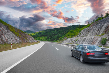 Wall Mural - Black car on asphalt road. Asphalt road view in countryside at beautiful sunset