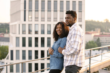 Poster - Young African American couple woman and man hugging on rooftop of modern building and looking away. Concept of love relationships and outdoors activity.