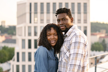 Wall Mural - Urban portrait of loving couple. African American people in love waking at evening on rooftop of modern building. Young girlfriend and boyfriend having date after work.