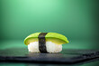 Close up of one piece of avocado nigiri wrapped around with a strip of Nori with green background